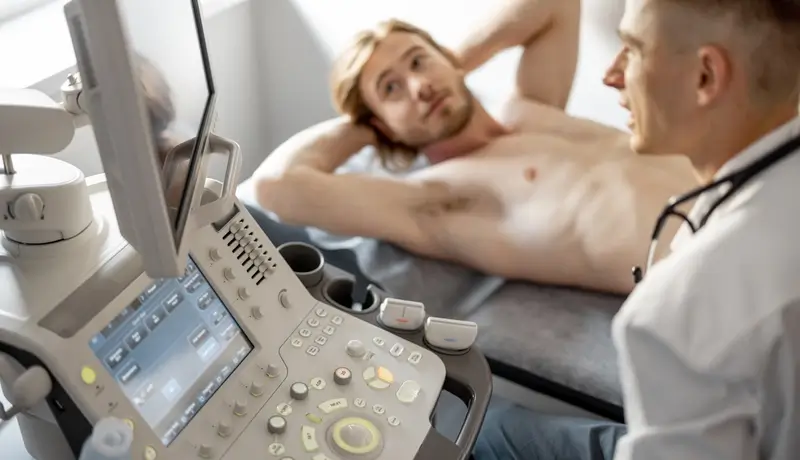 Doctor performing an abdominal ultrasound on a patient, showing medical equipment and patient interaction.
