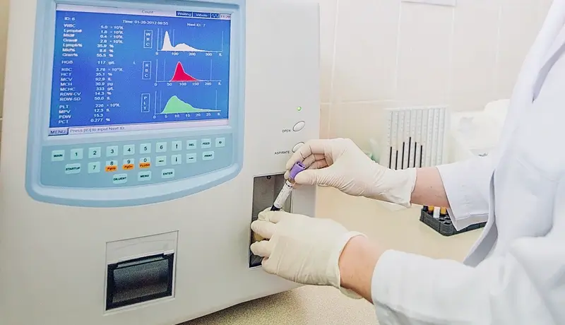 Laboratory technician using an automated blood analyzer to evaluate a sample for diagnostic purposes.