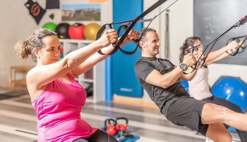 People performing suspension training exercises in a fitness studio, focusing on strength and endurance.