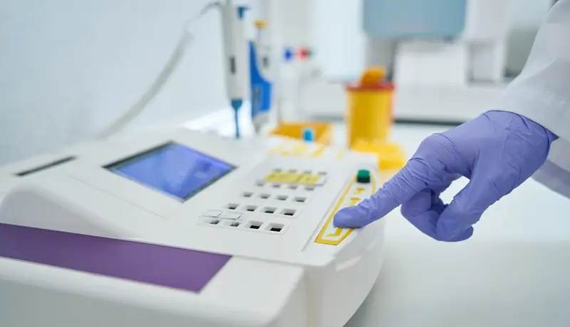 Gloved hand operating a laboratory analyzer, highlighting advanced diagnostic equipment used for medical testing.