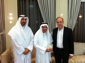 The president of homed along with two officials from Kuwait pose for a photo. The older of the two officials is holding a commemorative gift given to him by the president of homed.