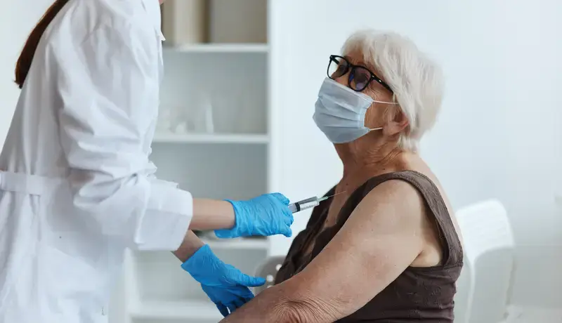 A healthcare professional administering a vaccine to an elderly woman wearing a face mask.