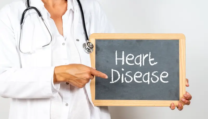 A doctor in a white coat pointing to a blackboard with the words "Heart Disease" written on it, emphasizing the importance of heart health.