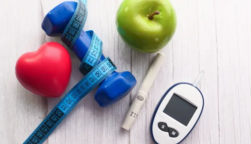 Hands preparing an insulin syringe on a table with a glucose meter, an insulin pen, and a plate of pink macarons, symbolizing the balance between diabetes management and dietary indulgence.