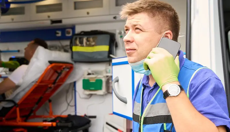 Paramedic communicating on a phone while assisting a patient in an ambulance, emphasizing emergency response coordination.
