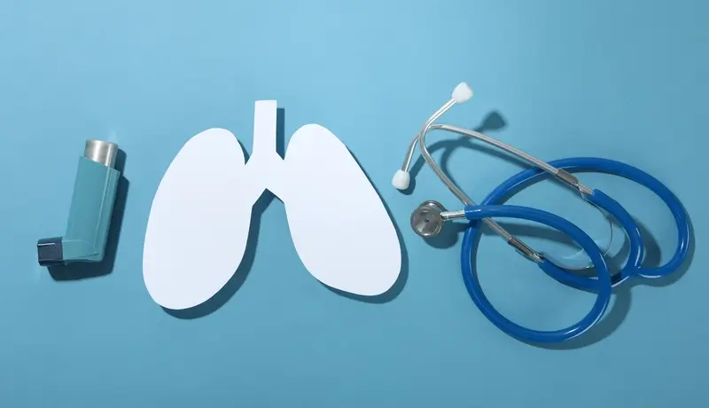Inhaler, lung diagram, and stethoscope on a blue background, symbolizing respiratory health.