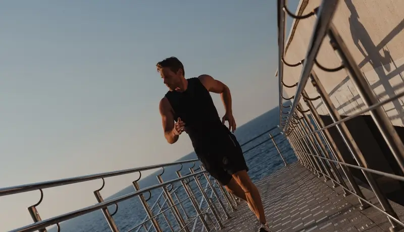Confident young man in sports clothing enjoying early morning jog with the sea on background