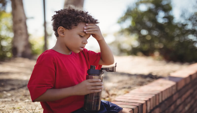 Dehydrated boy sitting with water bottle during obstacle course