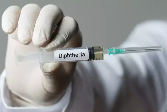 Σύριγγα με ετικέτα "Diphtheria" κρατημένη από χέρι ιατρού με γάντι.