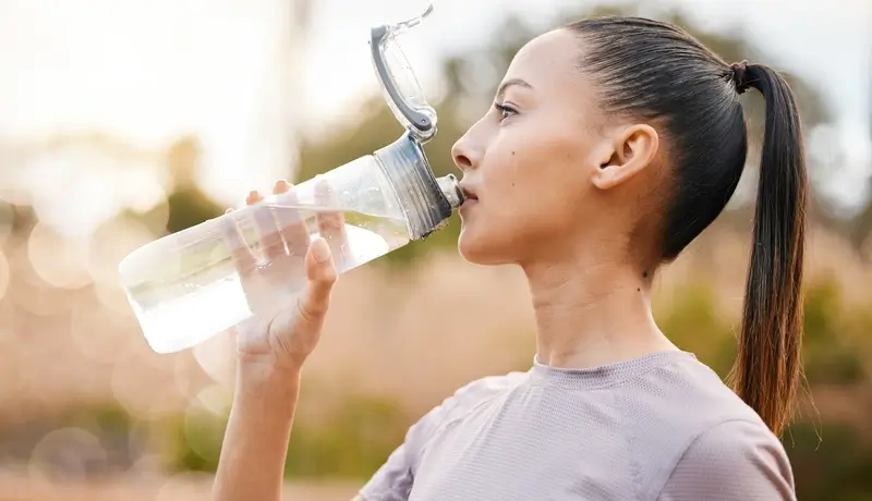 Fitness, health and woman drinking water in nature after exercise, training or workout.