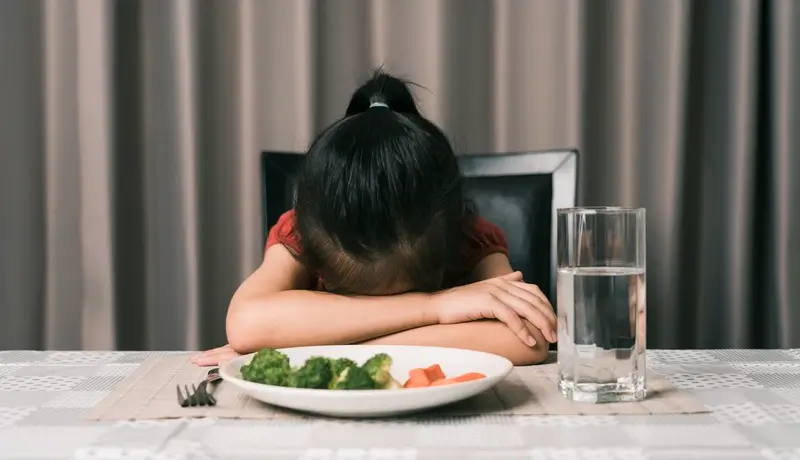 Little cute kid girl refusing to eat healthy vegetables. Children do not like to eat vegetables.
