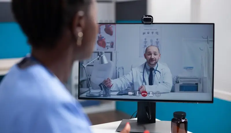 A healthcare professional consulting with a doctor via a telemedicine video call in a modern clinical setting.