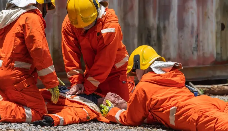 Rescue team performing CPR on an injured individual during a training exercise, wearing orange protective gear and helmets.