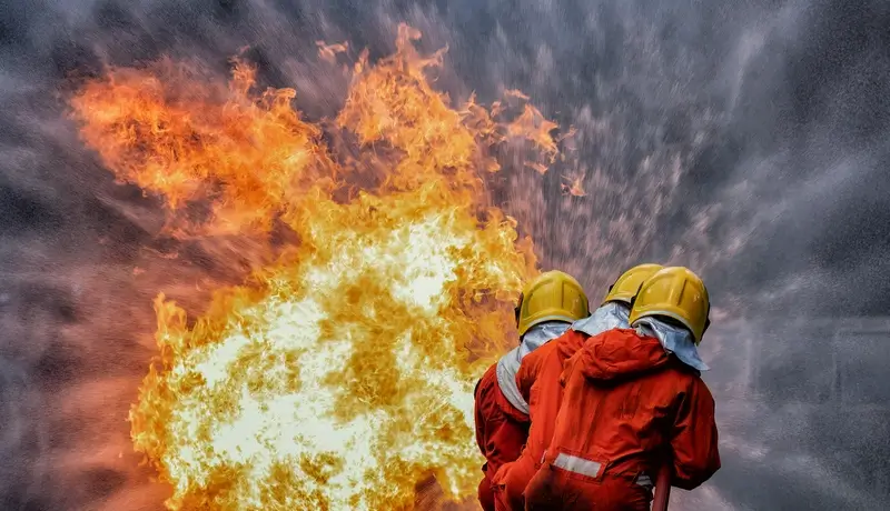 Firefighters battling intense flames during a fire emergency, wearing protective gear and helmets.