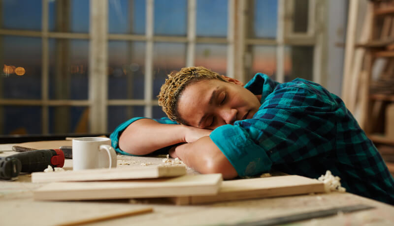 a man with blue jacket taking a nap on the office.
