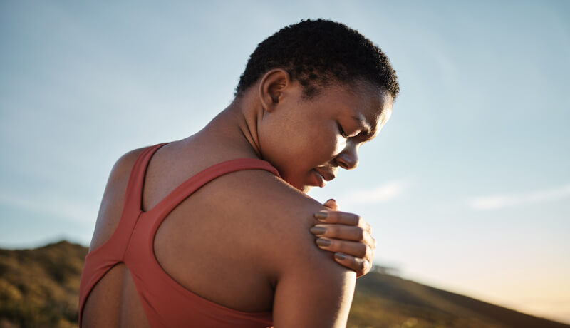 Shoulder, black woman and exercise injury from outdoor sports training on sky background. Athlete,
