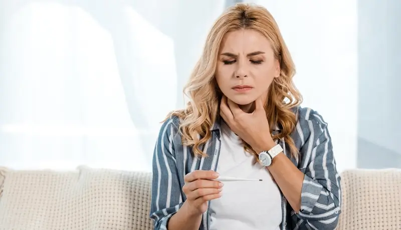 sick woman with sore throat and holding electronic thermometer