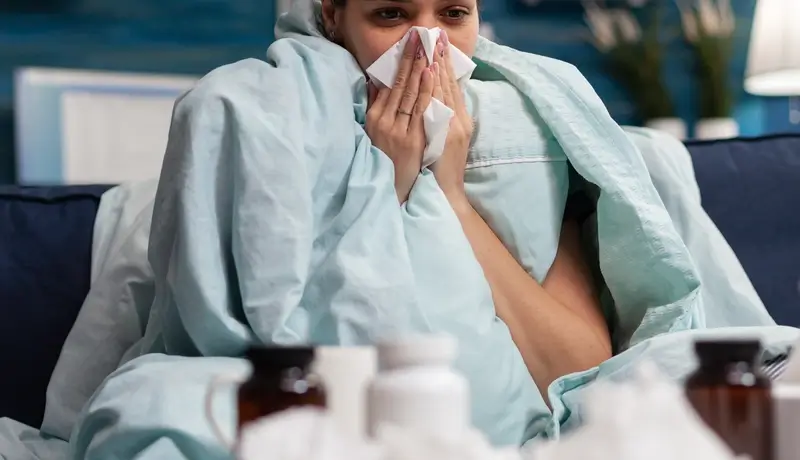 Sick woman wrapped in blanket at home