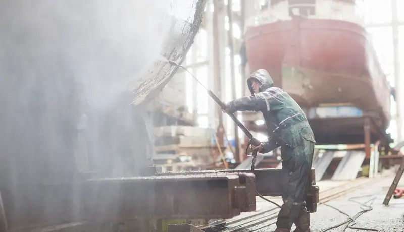 A maritime workerusing high pressure hose in order to wash the boat