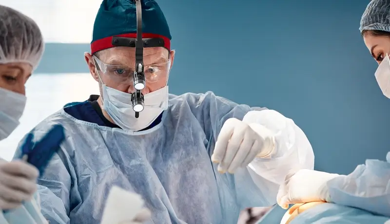 A surgeon wearing a headlamp performing a medical procedure with a team in a sterile operating room.